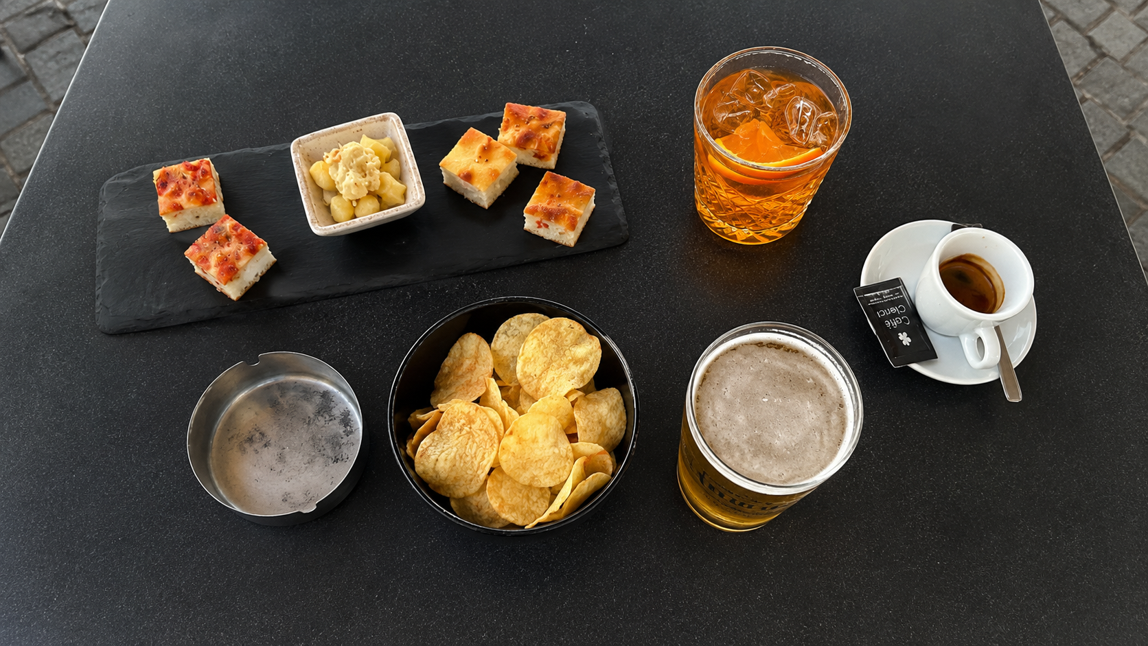 Aperitivo mit Spritz, Bier, Espresso und kleinen Snacks auf einem Cafétisch am Lago Maggiore.