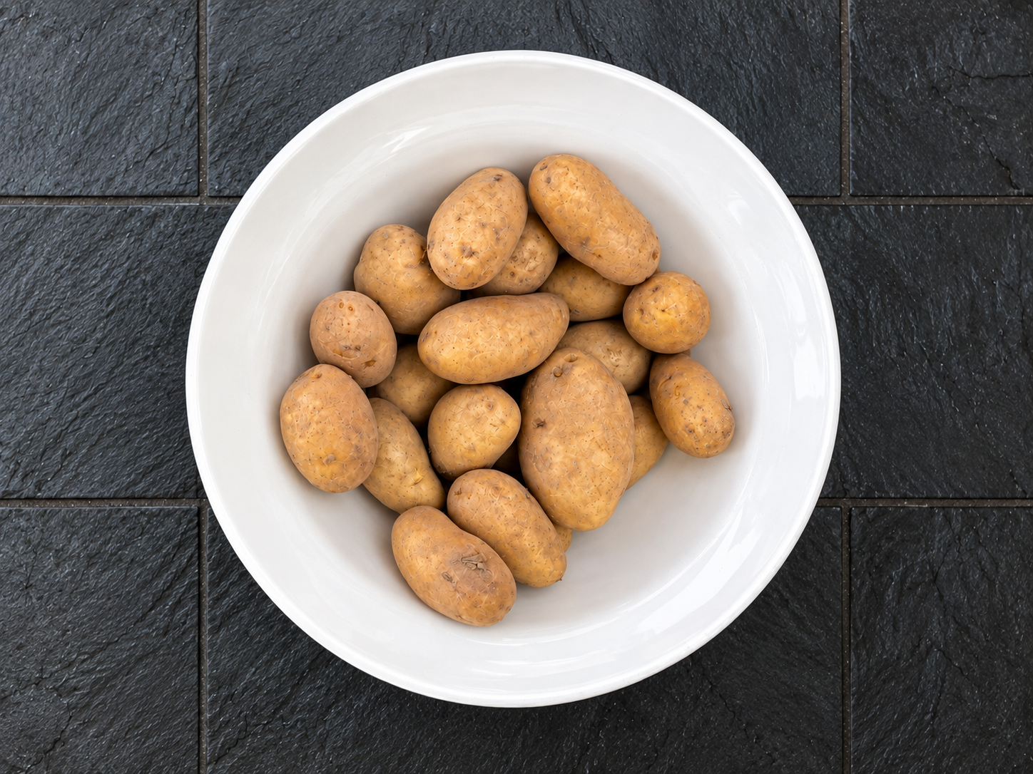 Kartoffeln in einer weißen Schüssel auf dunklem Schieferboden