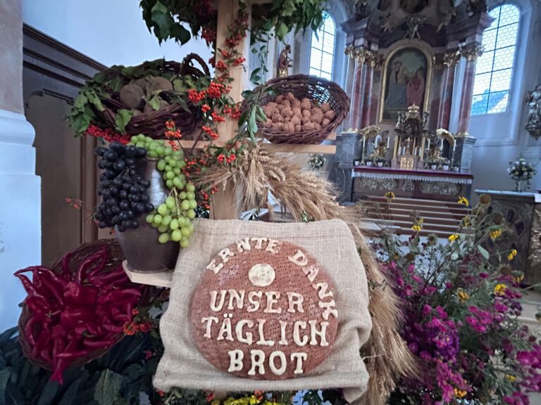 Erntedankbrot mit der Aufschrift „Ernte Dank – Unser täglich Brot“, umgeben von Getreide, Trauben, Nüssen und Blumen in St. Justina in Bad Wörishofen.